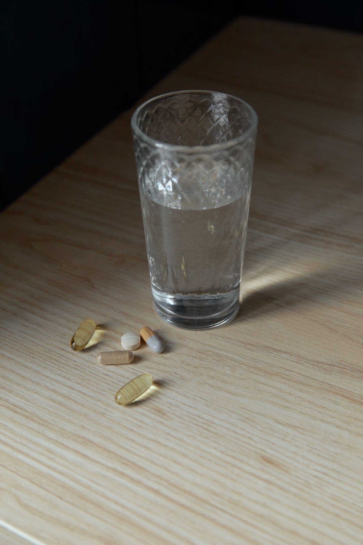 Et glas vand og nogle kapsler og tabletter på et lyst træbord